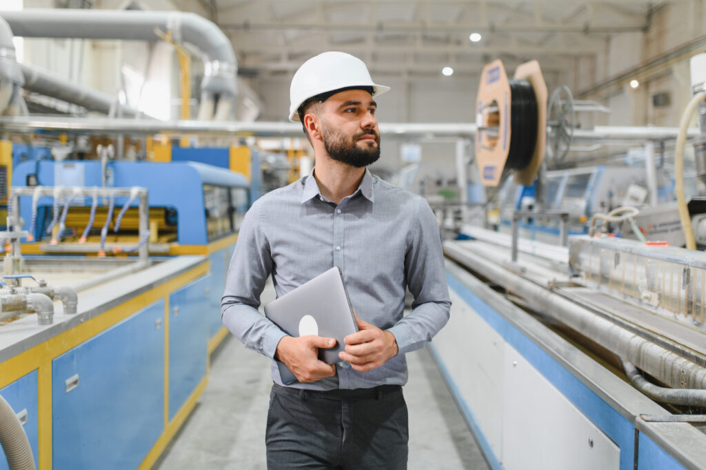 Industrial engineer in a hardhat reviewing data on a tablet on the manufacturing plant floor, illustrating sales enablement for manufacturing and enterprise account planning