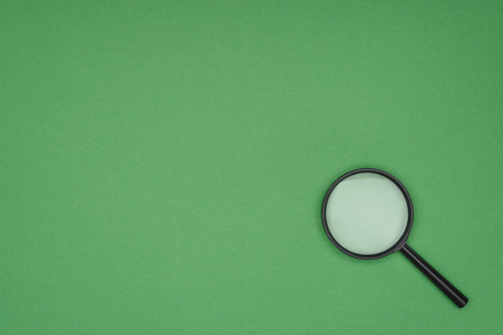 Magnifying glass resting on a green background representing research and discovery
