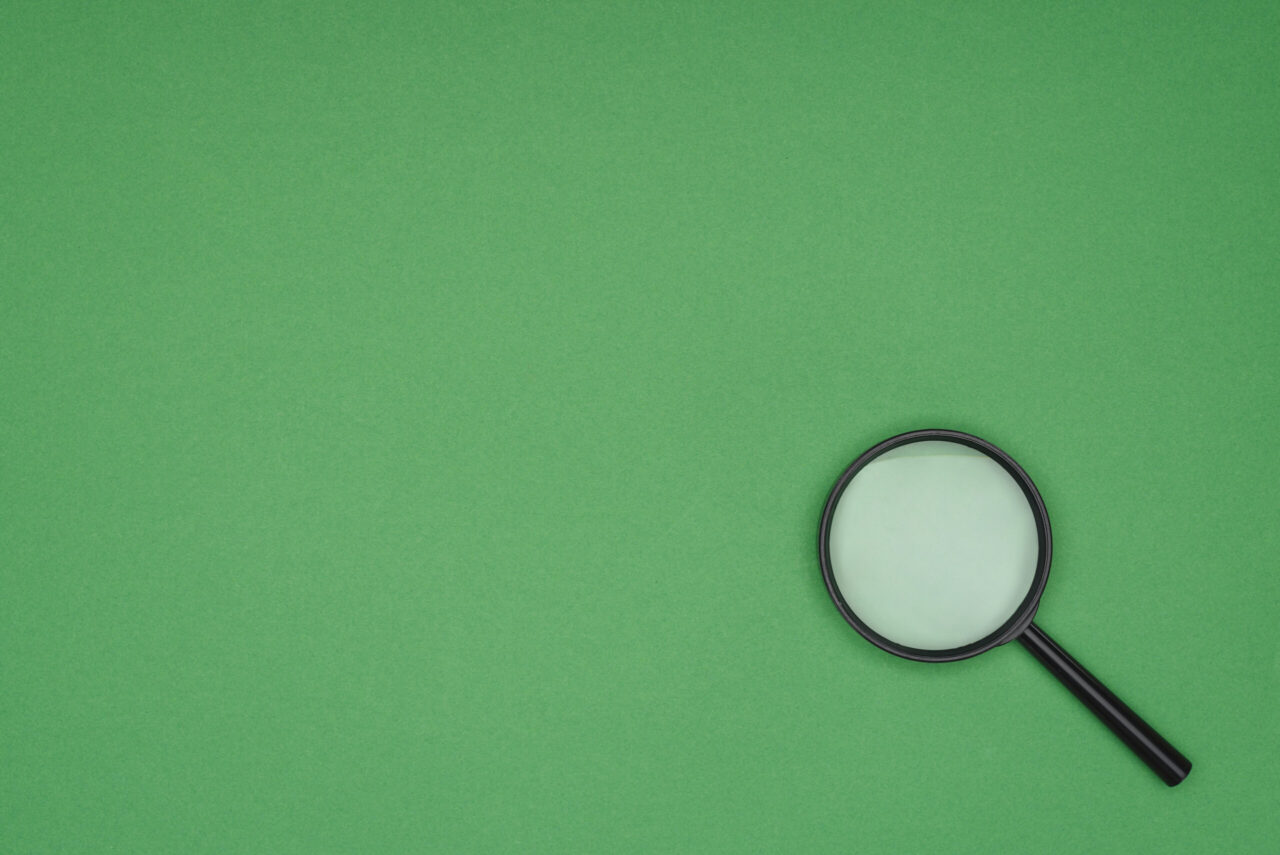 Magnifying glass resting on a green background representing research and discovery