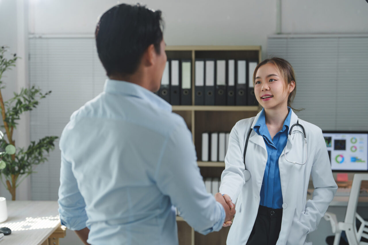 Doctor in a white coat shaking hands with a person in a medical office