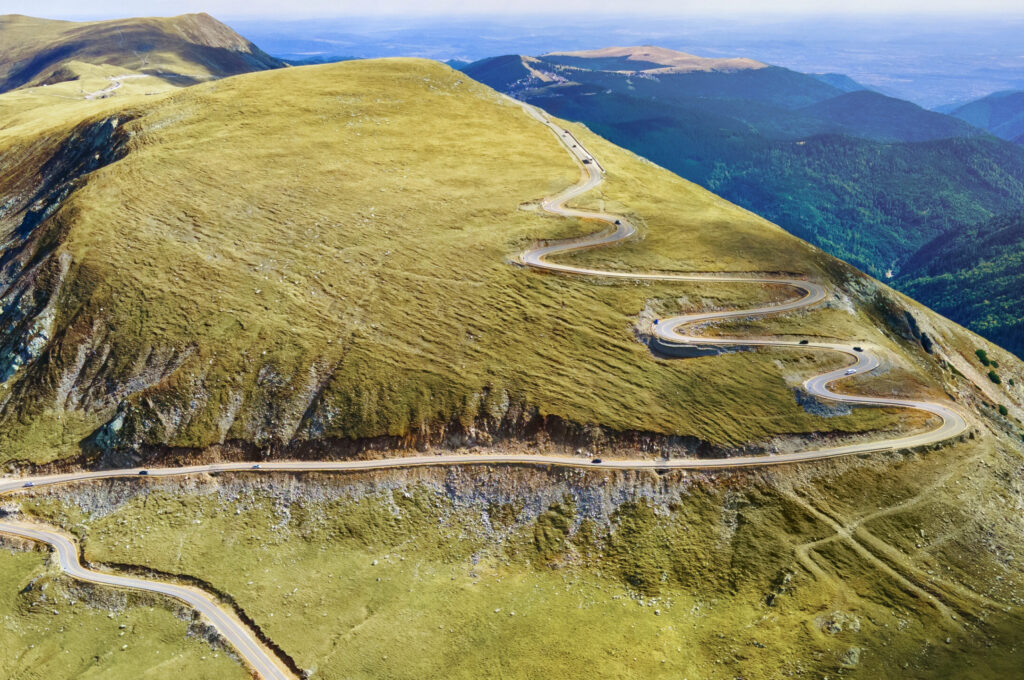 Aerial view of a winding mountain road curving through green hills
