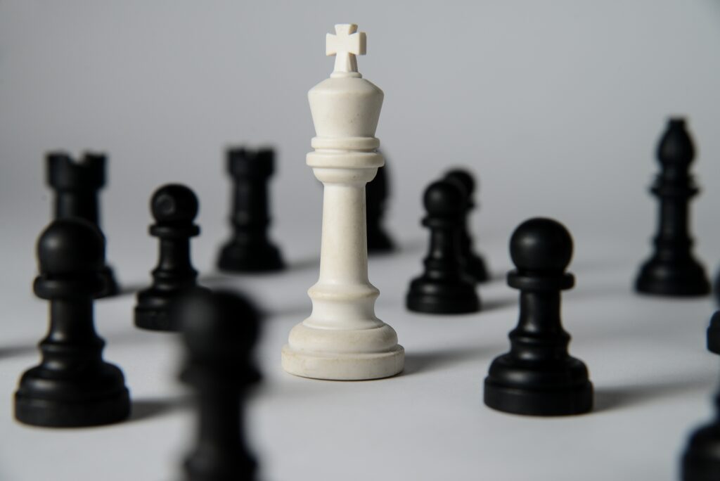 White chess king standing among fallen black chess pieces