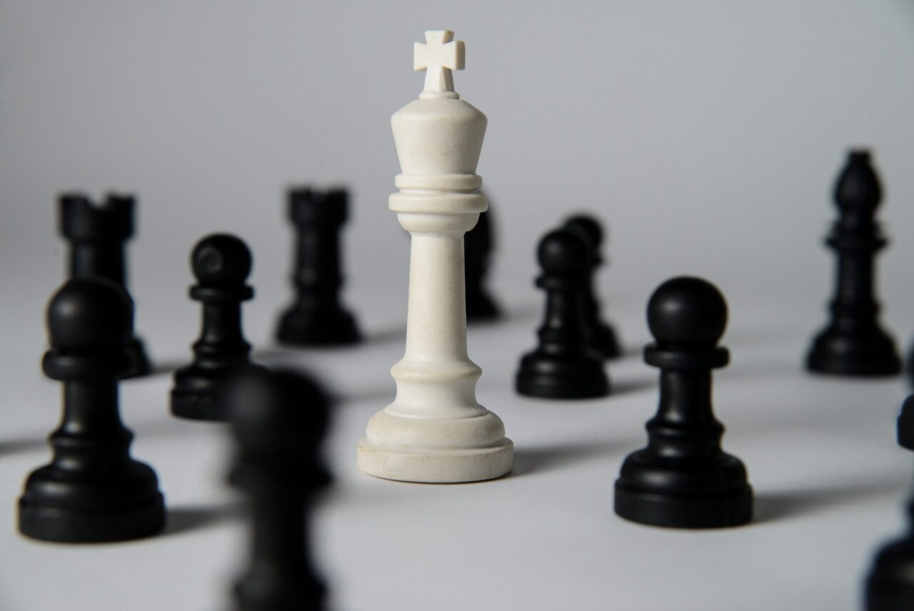 White chess king standing among fallen black chess pieces