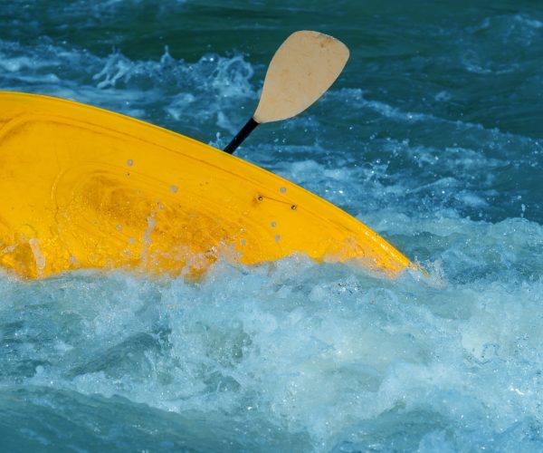 Canoer in a yellow kayak flipping over in strong rapids